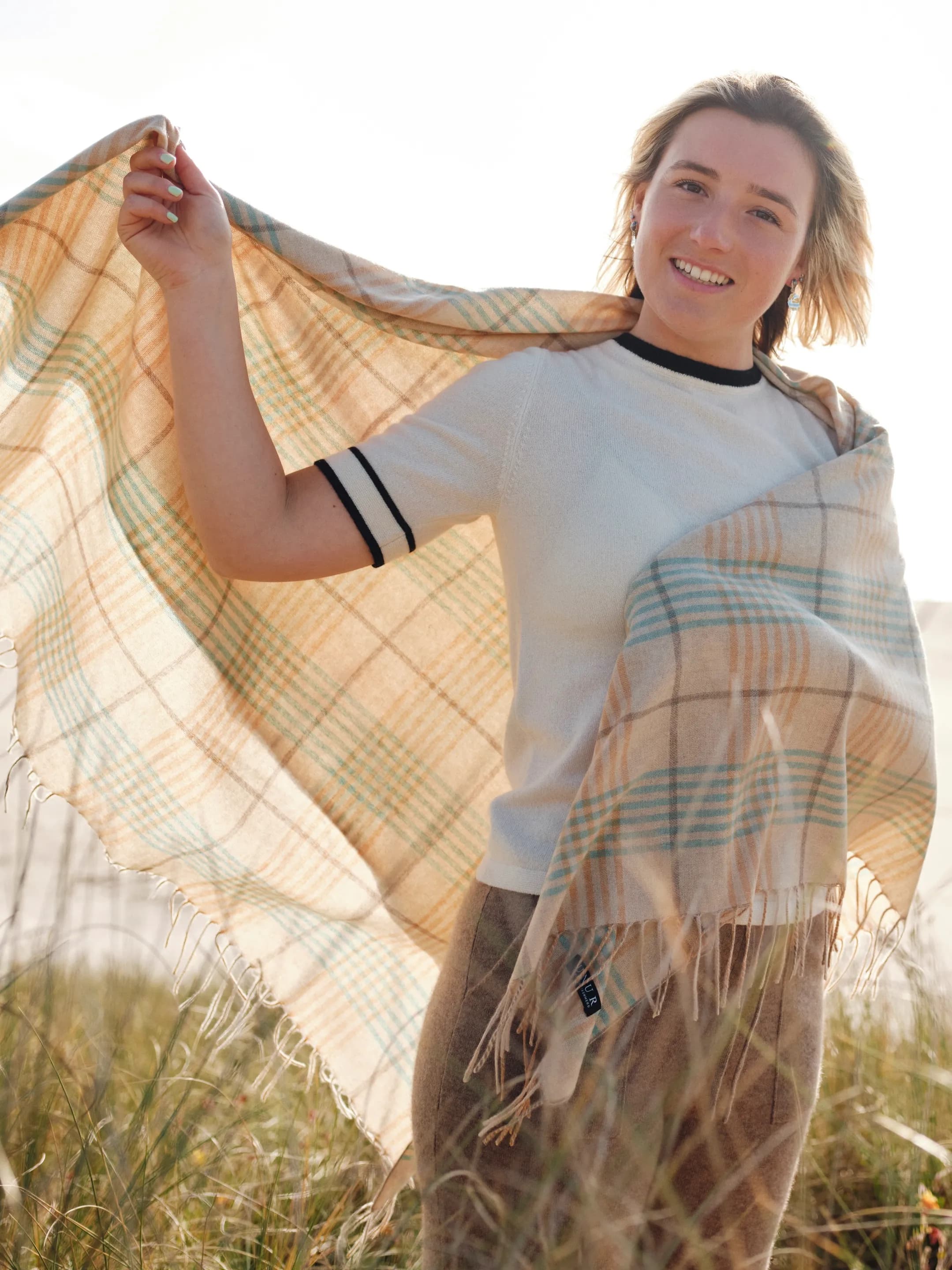 Model outdoors wearing a cashmere plaid wrap shawl with tasselled edges